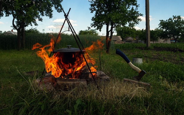 Olla de cocción en fogata y hacha de troncos al aire libre