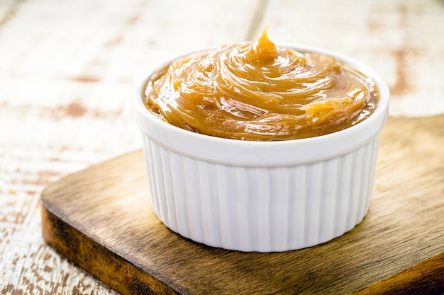 Olla de dulce de leche o caramelo casero sobre fondo de madera rústica, dulce típico brasileño