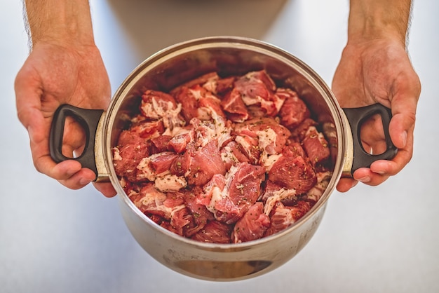 olla llena de trozos de carne cruda en manos del cocinero.