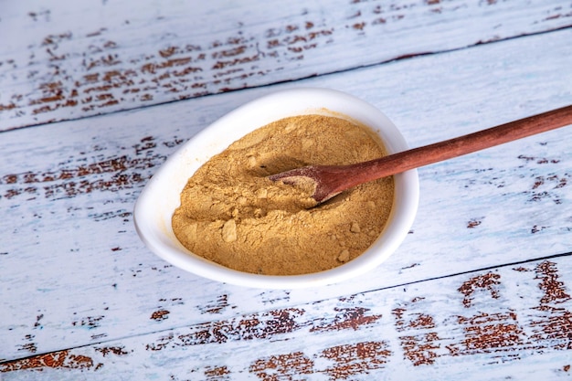 Olla con polvo de maca peruana y cuchara de madera rústica sobre un fondo de madera blanca