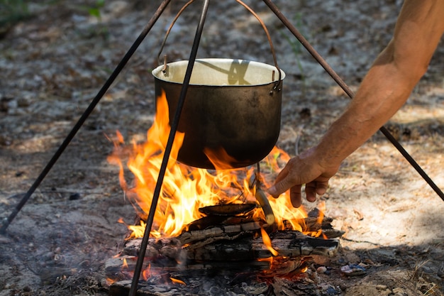 Olla turística colgando sobre el fuego en un trípode. Cocinando en la campaña.