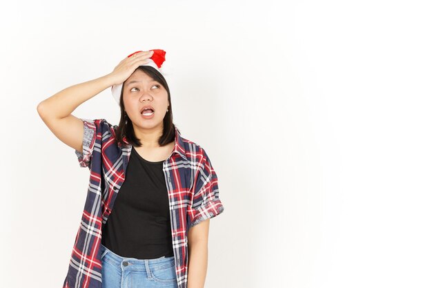 Olvídese de algo gesto de mujer asiática con camisa a cuadros roja y gorro de Papá Noel aislado en blanco