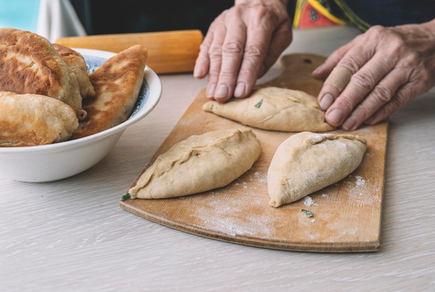 Oma kocht Kuchen. Hausgemachtes Essen. Omelettkuchen aus dem Teig in den Händen der Frauen. Der Prozess der Herstellung von Tortenteig von Hand