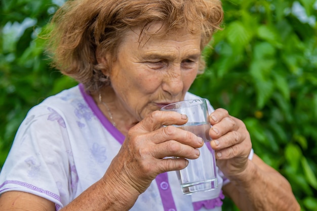 Oma trinkt Wasser aus einem Glas. Selektiver Fokus. Frau.