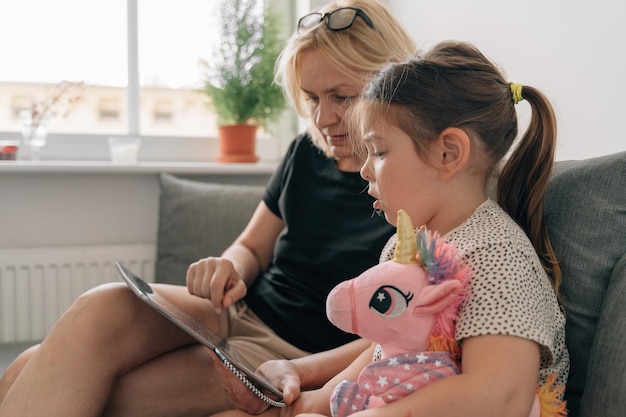 Oma und Vorschulmädchen mit Tablet zusammen zu Hause auf dem Sofa Zeit für Familienzusammengehörigkeit