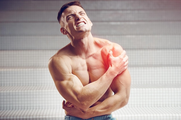 Foto ombro ferido jovem atleta musculoso bonito com dor no ombro conceito de fitness e saúde esportivo