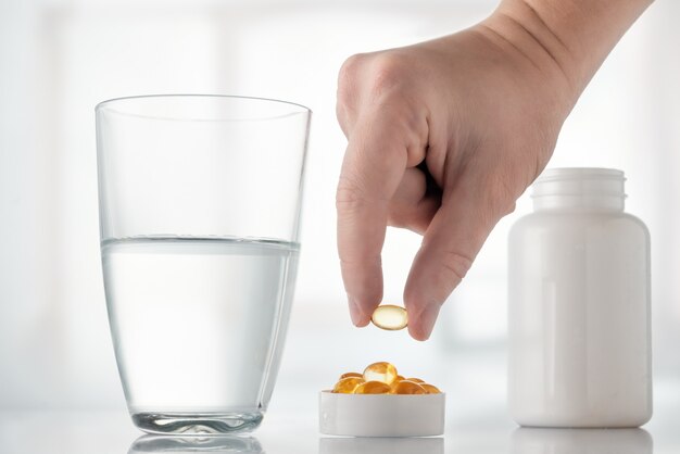 Omega 3, grasa de pescado, aminoácidos y un vaso de agua sobre la mesa.