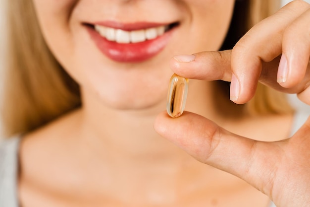 Omega-3-Pille aus Fischfettöl in der Nähe der Lippen, Nahaufnahme BADS-Kapsel mit biologisch aktiven Nahrungsergänzungsmitteln Vitamin D für den Aufbau und Erhalt gesunder Knochen