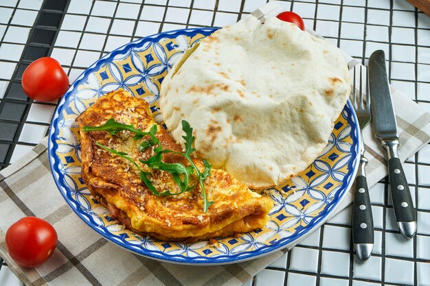 Omelete assado com parmesão e rúcula com pão de focaccio em uma placa de cerâmica incomum em uma composição com ingredientes close-up vista. Lay plana de alimentos