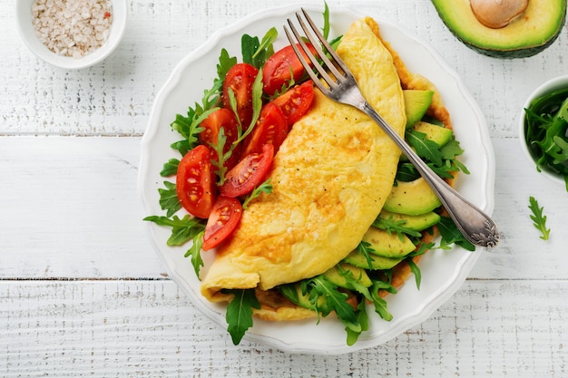 Omelete com abacate, tomate e rúcula em prato de cerâmica branco sobre superfície de pedra clara