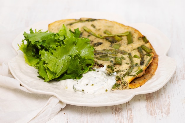 Omelete com aspargos, salada fresca e molho no prato branco