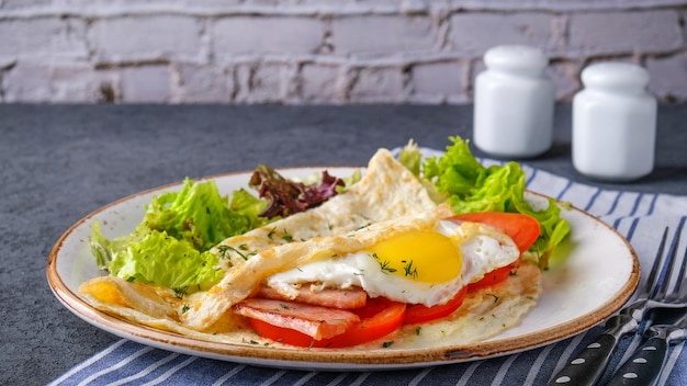 Omelete com bacon de ovo frito e tomate em um prato servido com garfo e faca Conceito de café da manhã saboroso