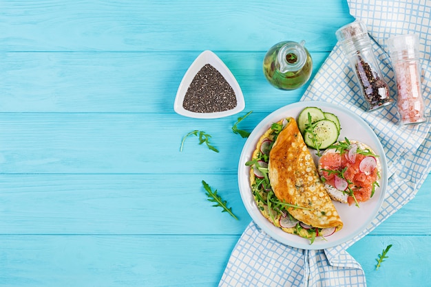 Omelete com rabanete, rúcula verde e sanduíche com salmão no prato branco