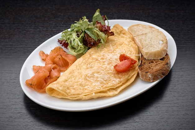 Omelete com salmão, ervas e torradas de ciabatta, em superfície escura