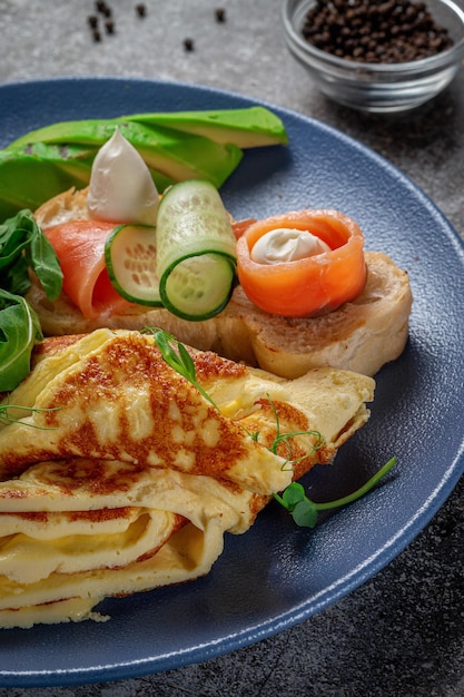 Omelete com salmão, ervas frescas e tomates em um prato azul com especiarias em uma mesa de pedra cinza