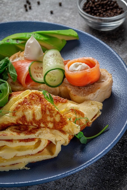 Foto omelete com salmão, ervas frescas e tomates em um prato azul com especiarias em uma mesa de pedra cinza