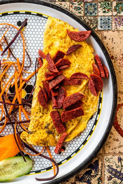 Omelete com salsicha e legumes em chapa branca.