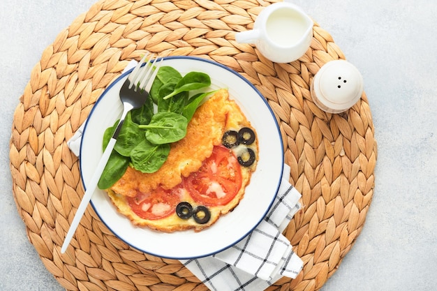 Omelete com tomate azeitonas pretas queijo cottage e ervas de espinafre verde na chapa branca sobre fundo cinza de concreto Delicioso café da manhã Comida de café da manhã saudável Vista superior