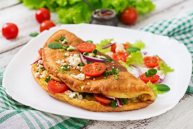 Omelete com tomate, salsa e queijo feta na chapa branca.