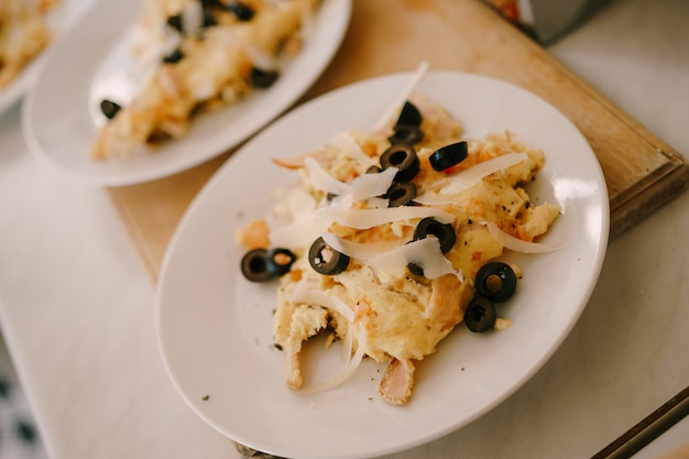 Omelete de ovo com queijo e azeitonas pretas em um prato branco sobre a mesa