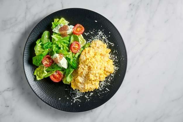 Omelete mexido com salada de espinafre, ricota e tomate cereja, servido em prato preto sobre mármore