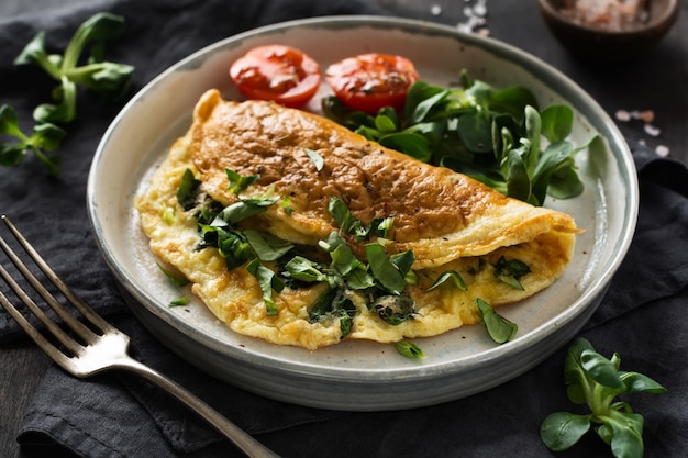 Omelete recheado com tomate, pimentão vermelho, cream cheese e milho ou alface de cordeiro em madeira escura com espaço de cópia. Comida de dieta saudável no café da manhã.