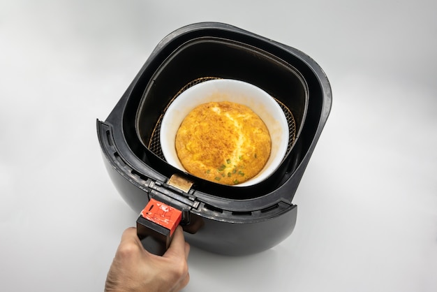 Foto omelett in der weißen keramikschale innerhalb des schwarzen airfryers lokalisiert auf weißer oberfläche.