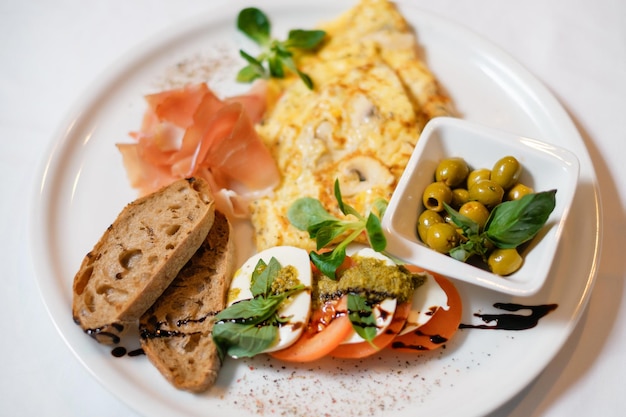 Omelett mit Croutons, Speck, Tomaten, Oliven, garniert mit Sojasauce, Senf und Basilikum Das Konzept eines köstlichen, herzhaften, hausgemachten Frühstücks, das in einem Restaurant serviert wird