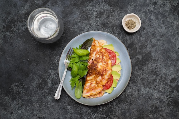 Omelett mit Käse und Kräutern mit einem Glas Wasser auf dunklem Hintergrund