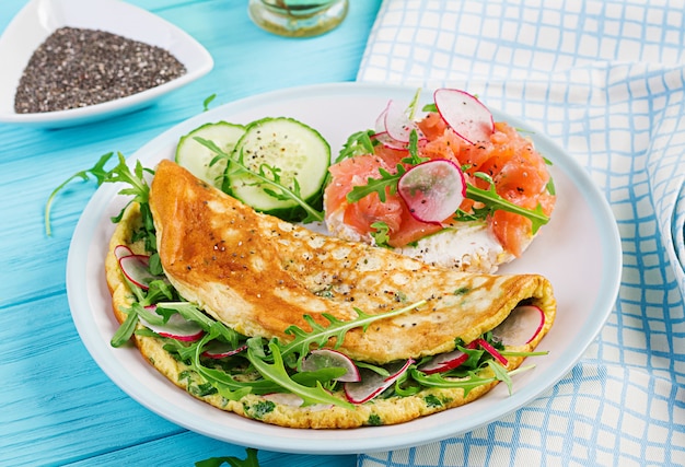 Omelett mit Radieschen, grünem Rucola und Sandwich mit Lachs auf weißem Teller