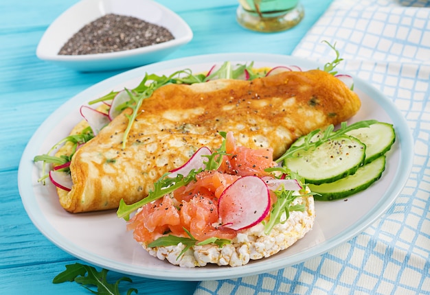 Omelett mit Radieschen, grünem Rucola und Sandwich mit Lachs auf weißem Teller