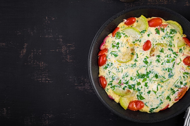 Omelett mit Tomaten, Zucchini und roter Zwiebel auf dunkler Tabelle. Frittata - italienisches Omelett. Ansicht von oben