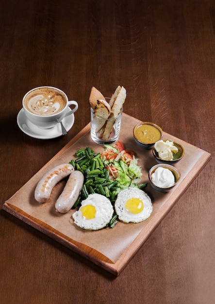 Omelett mit Würsten und Gemüse auf Holztisch. Kaffee in der weißen Tasse. Englisches Frühstück