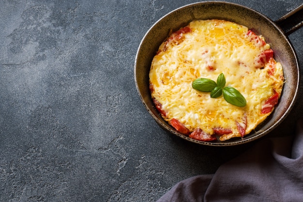 Omelett, Rührei mit Tomaten und Käse in einer Pfanne auf einem dunklen Tisch.