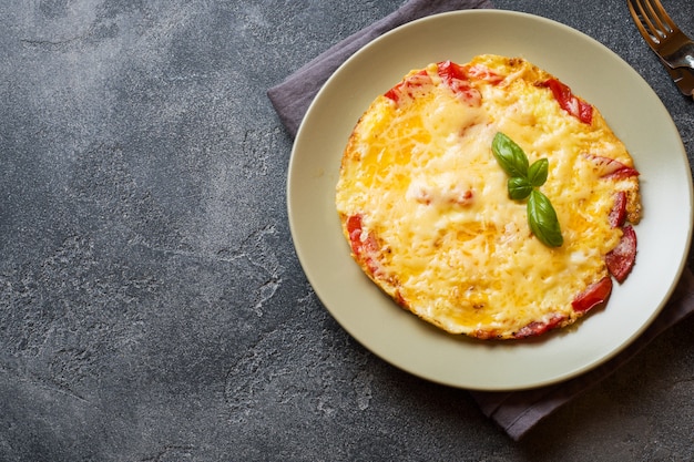 Omelett, Rührei mit Tomaten und Käse in einer Platte auf einer dunklen Tabelle.