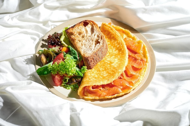 Omelette mit Lachs-Gemüse-Salat und Toast in einem Teller auf einem weißen Blatt Tough Light