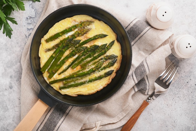 Omelette mit Spargel Frittata oder Rührei mit Spargel in der Pfanne mit Petersilie und Pfeffer auf grauem Betontischhintergrund Nützliches Frühstückskonzept Draufsicht