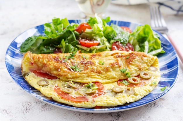 Omelette mit Tomaten, grünen Oliven und frischem Salat auf blauem Teller Frittata italienisches Omelett