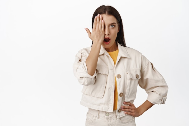 Omg, olhe. mulher impressionada e surpresa com metade de um olho no rosto, mandíbula caída e ofegante, chocada e espantada por smth incrível, de pé no branco.