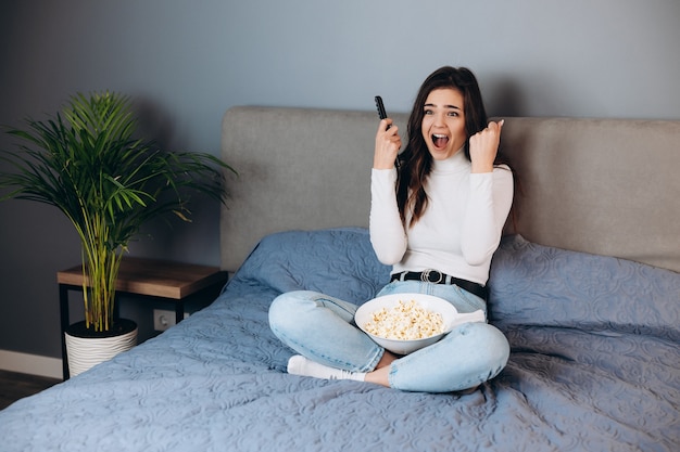 Omg was ist das. Erschrockene Frau schreit. Hübsche Frau hat Quarantäne-Freizeit Film ansehen beeindruckt überrascht unerwartetes Thriller-Filmende halten große Popcorn-Box sitzen Sofa im Haus drinnen.