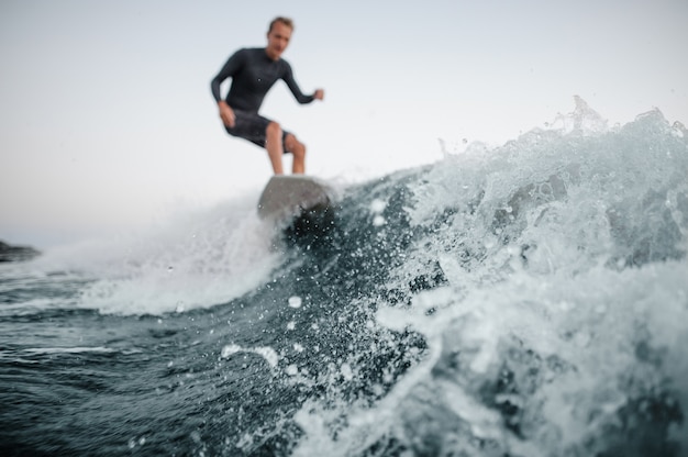 Onda azul en foco en primer plano con un hombre wakesurfing