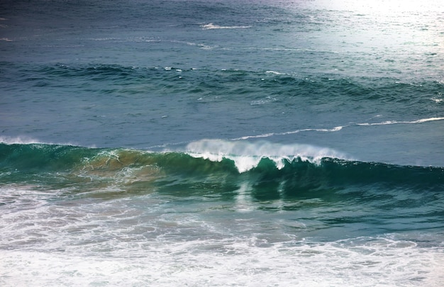 Onda azul na praia. Desfoque de fundo e manchas de luz solar. Fundo natural tranquilo.