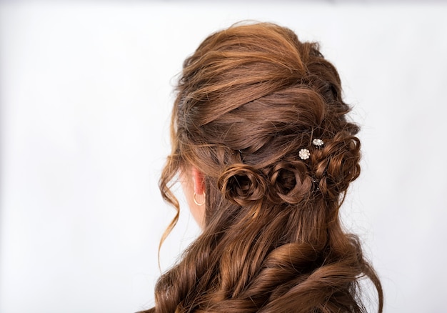 Onda cachos penteado. Penteado na mulher de cabelo castanho vermelho com cabelos longos, sobre um fundo branco. Serviços profissionais de cabeleireiro. Estilo de cabelo, trança com gancho de cabelo.