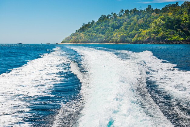 Onda de barco de cruzeiro na superfície da água e horizonte com mar azul e costa da ilha ao fundo