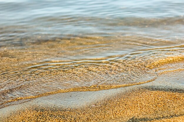 Onda que fluye en la playa de arena del mar al atardecer. Fondo de vacaciones de verano y concepto de naturaleza costera