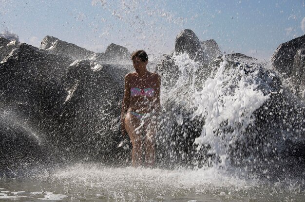 Foto ondas a salpicarem uma mulher sentada em rochas no mar.