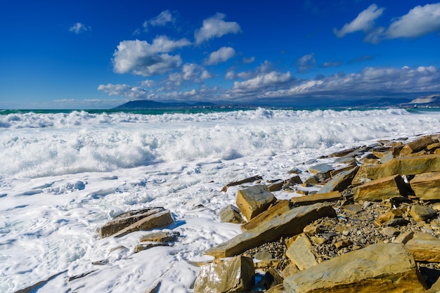 Ondas de tempestade em espuma branca quebram na praia repleta de fragmentos de rochas de arenito amarelado