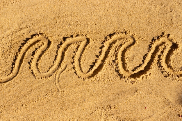 Foto ondas desenhadas na areia. chinelo e folhas. conceito de férias da praia de verão.