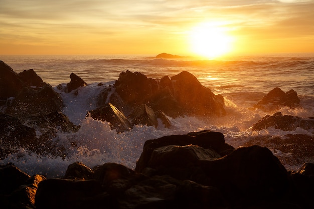 Ondas do mar batendo nas rochas no pôr do sol na Costa do Pacífico