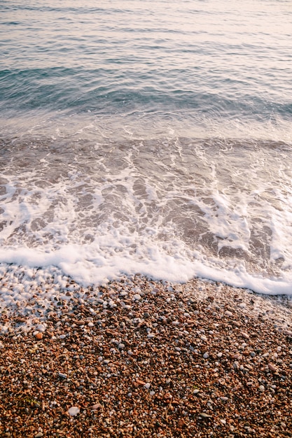 Ondas do mar com seixos laranja na praia